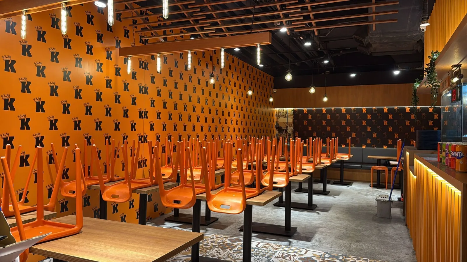 The dining room of a King of Fried Rice restaurant-format outlet, with orange chairs and crowned-K wallpaper