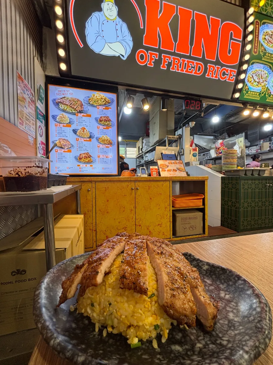 A plate of pork cutlet egg fried rice in front of a lit King of Fried Rice signboard and queue-number display